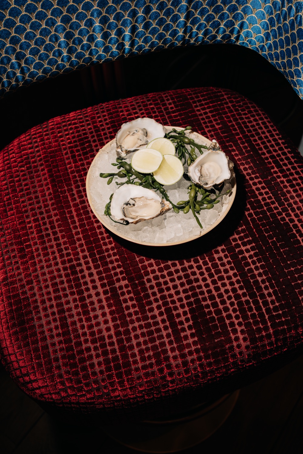 Fresh oysters on ice with lime slices, served on a red velvet chair