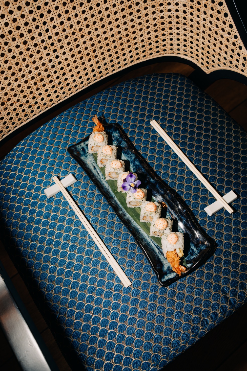 Sushi rolls on a blue patterned chair with chopsticks on the side