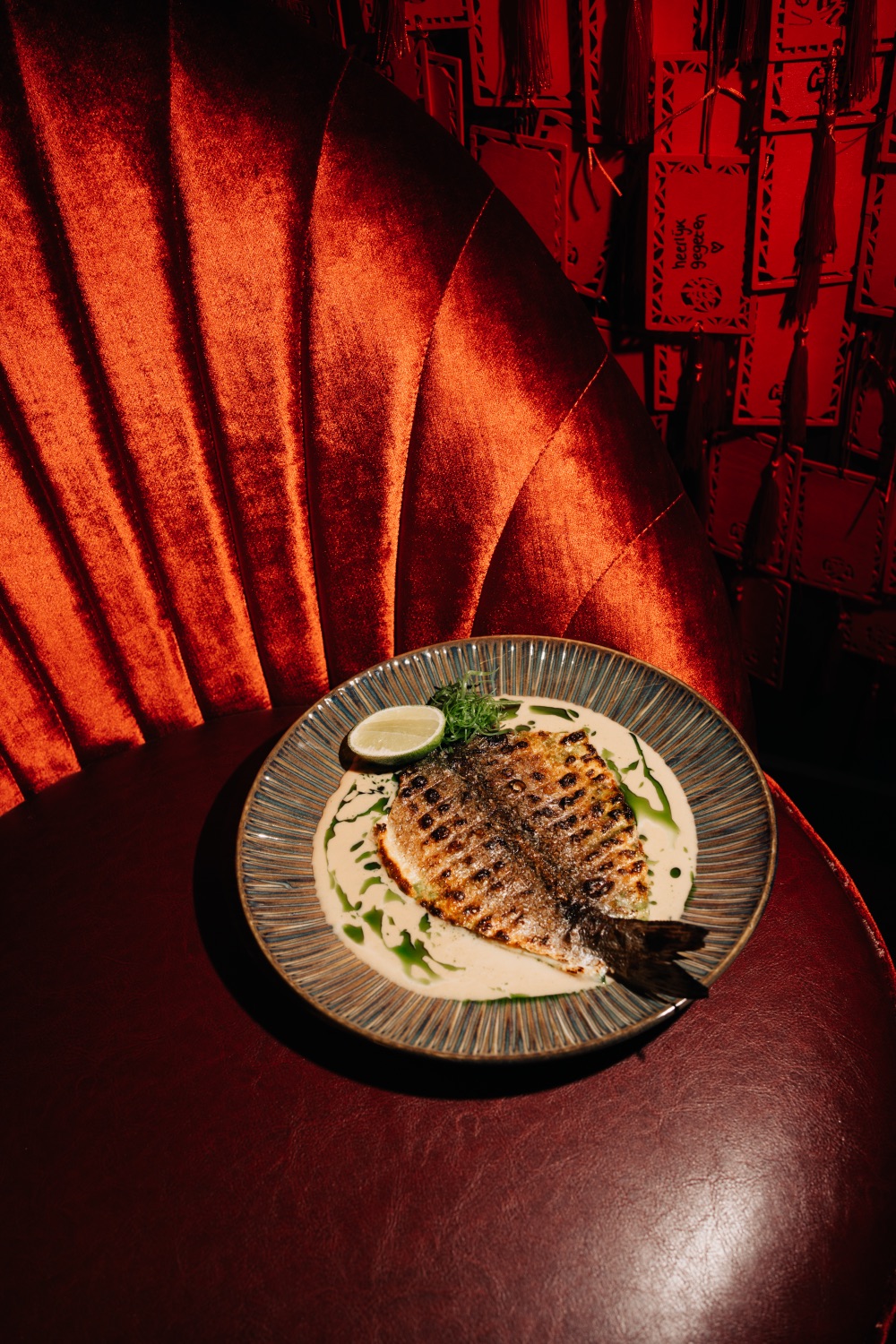 Grilled whole fish with creamy sauce and lime, served next to a red velvet booth