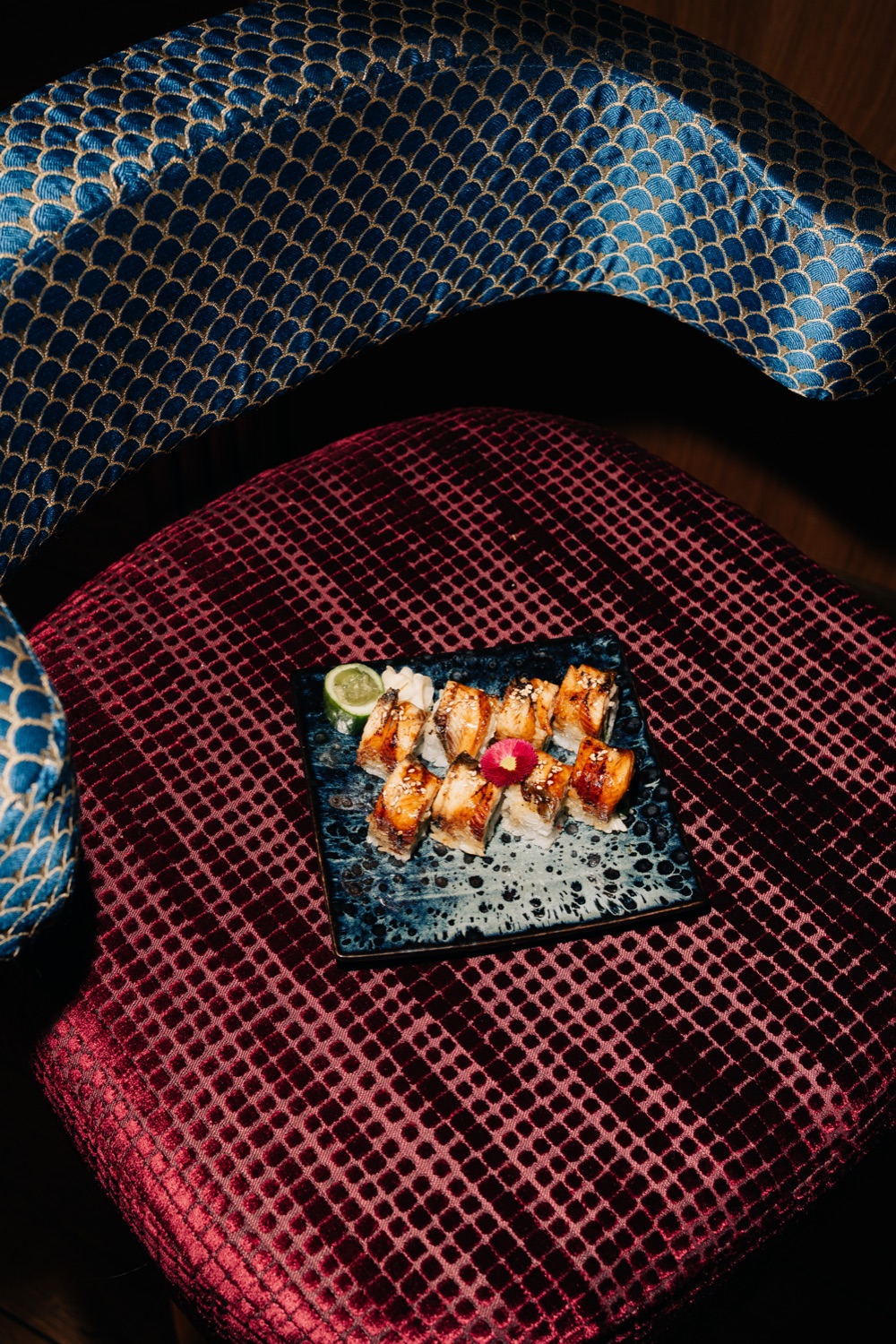 Eel sushi rolls on a blue plate placed on a red velvet chair