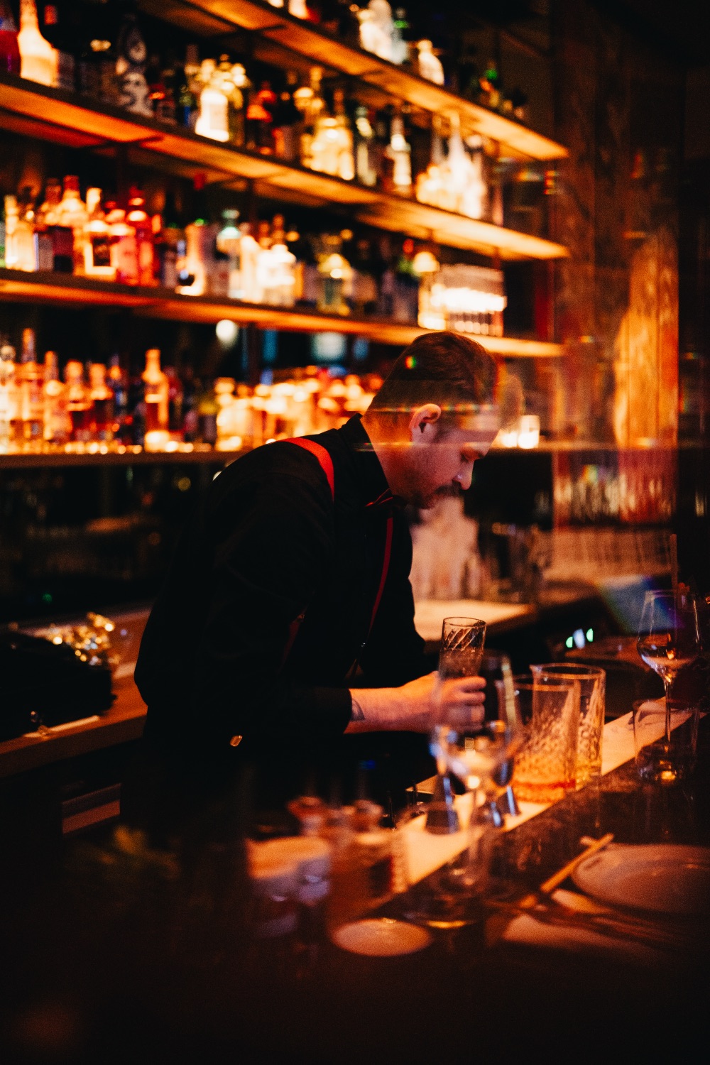 Bartender preparing a cocktail behind a dimly lit bar with glowing shelves of bottles