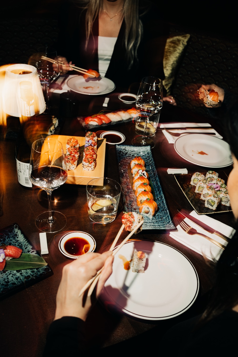 Friends sharing sushi platters and wine at a dimly lit restaurant table