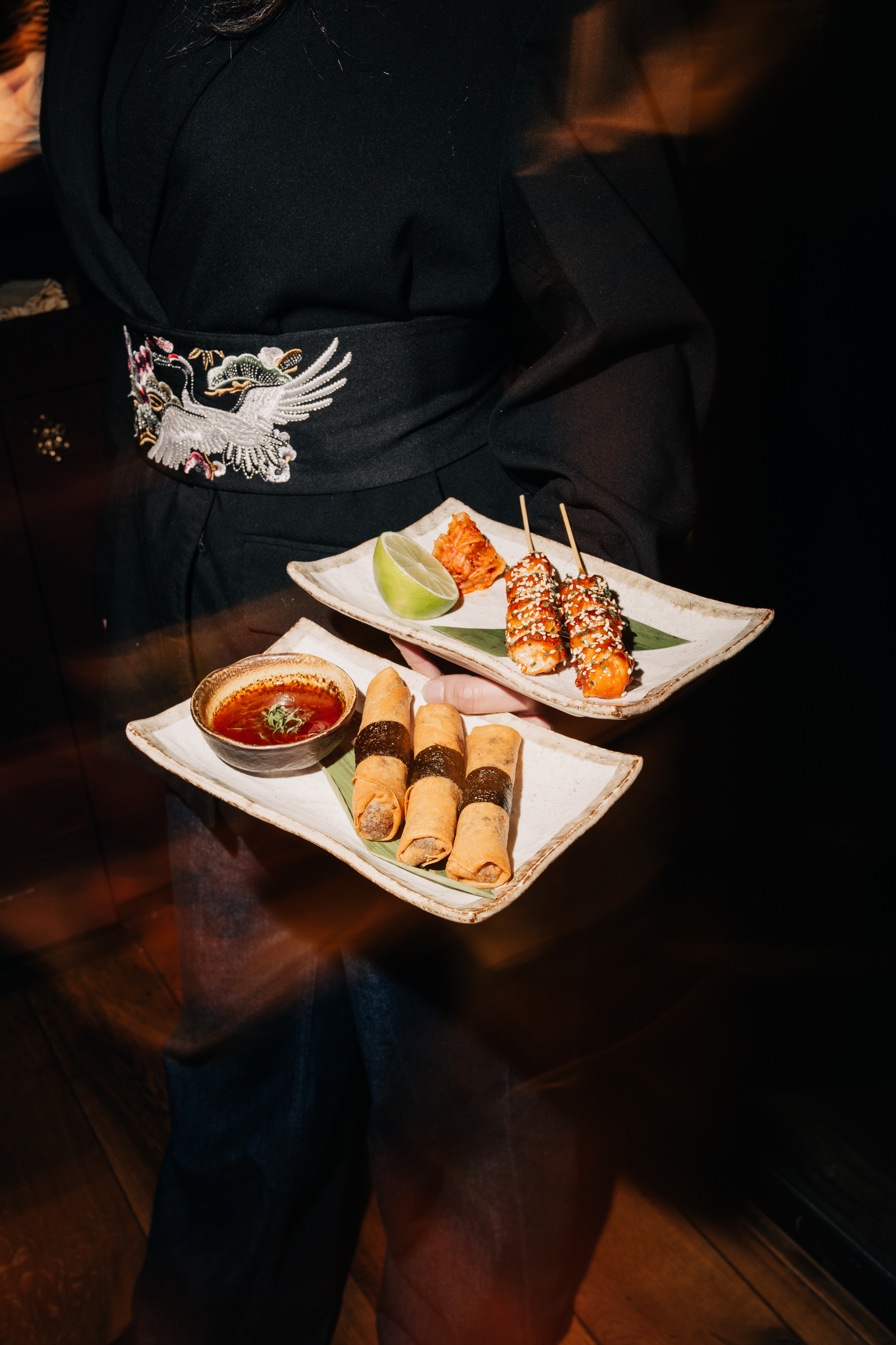 Server holding plates of spring rolls and skewers in a restaurant