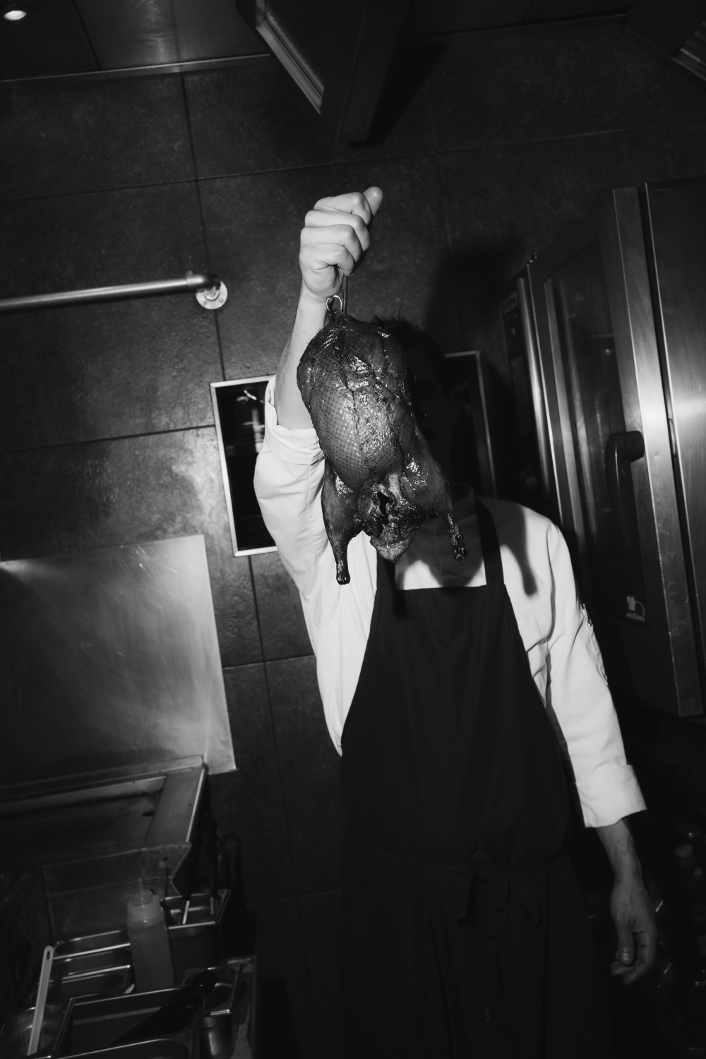 Black and white photo of a chef holding up a whole roasted duck