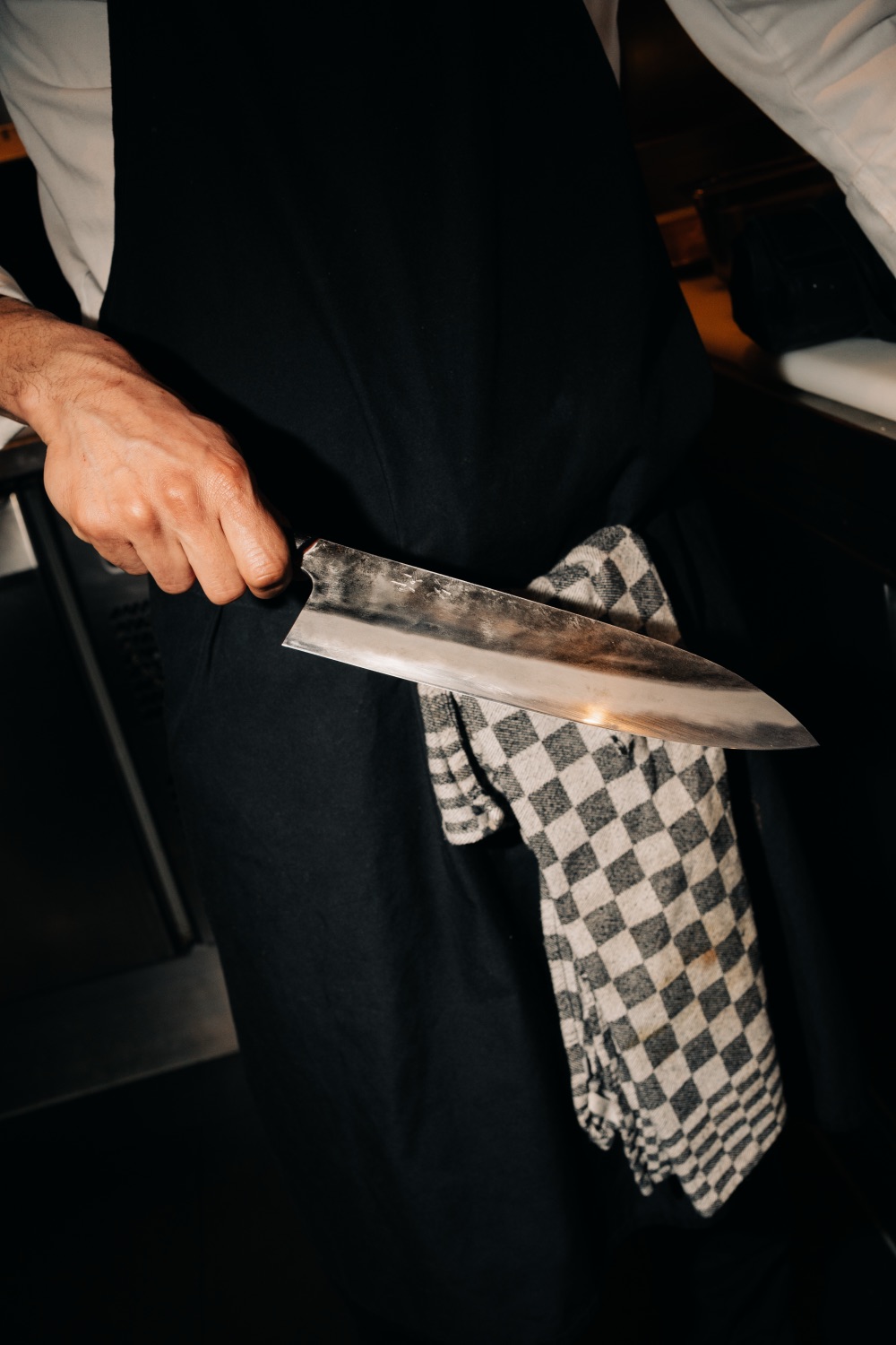 Close-up of a chef in a black apron holding a large kitchen knife
