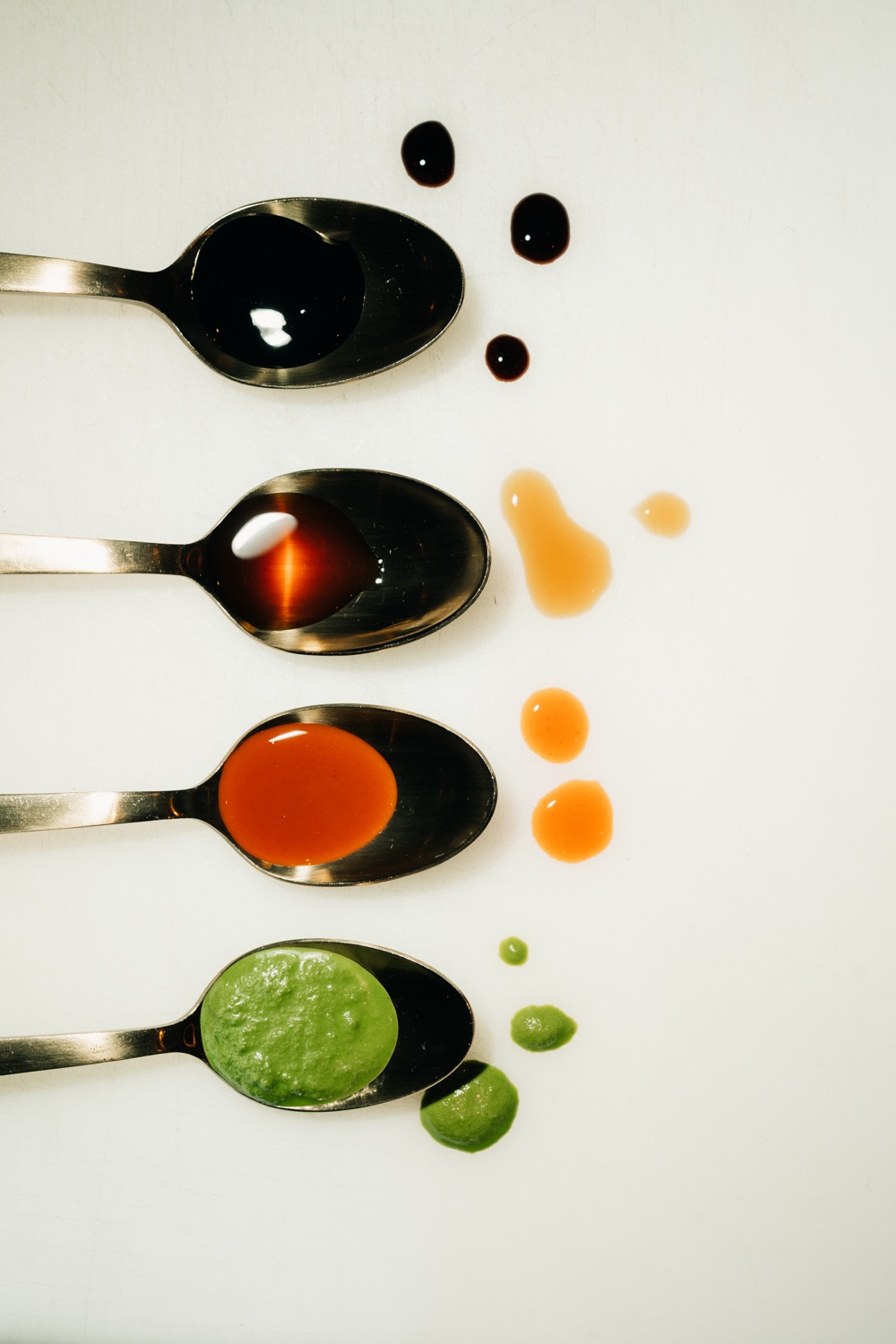 Four spoons filled with different colored sauces on a white background