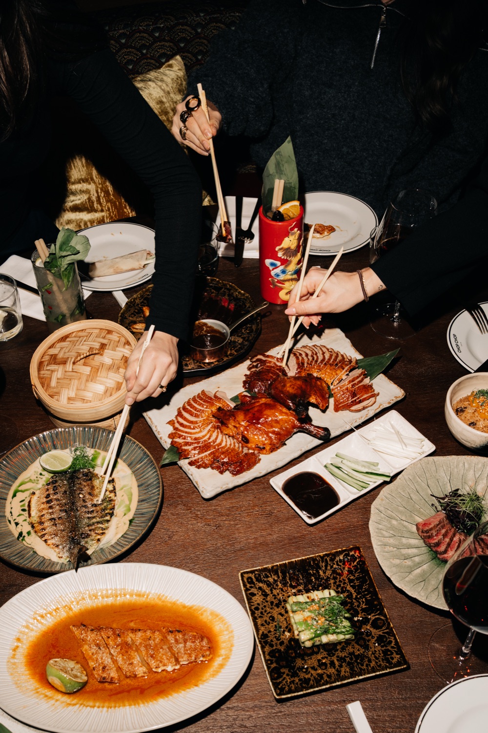 Guests using chopsticks to share Peking duck and other dishes at a restaurant table