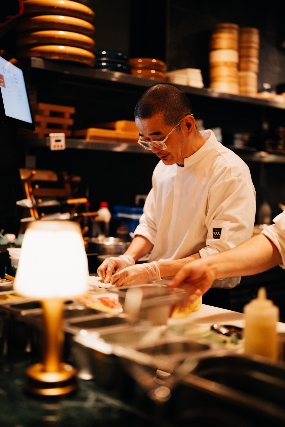 Sushi chef wearing glasses and gloves preparing food in an open kitchen