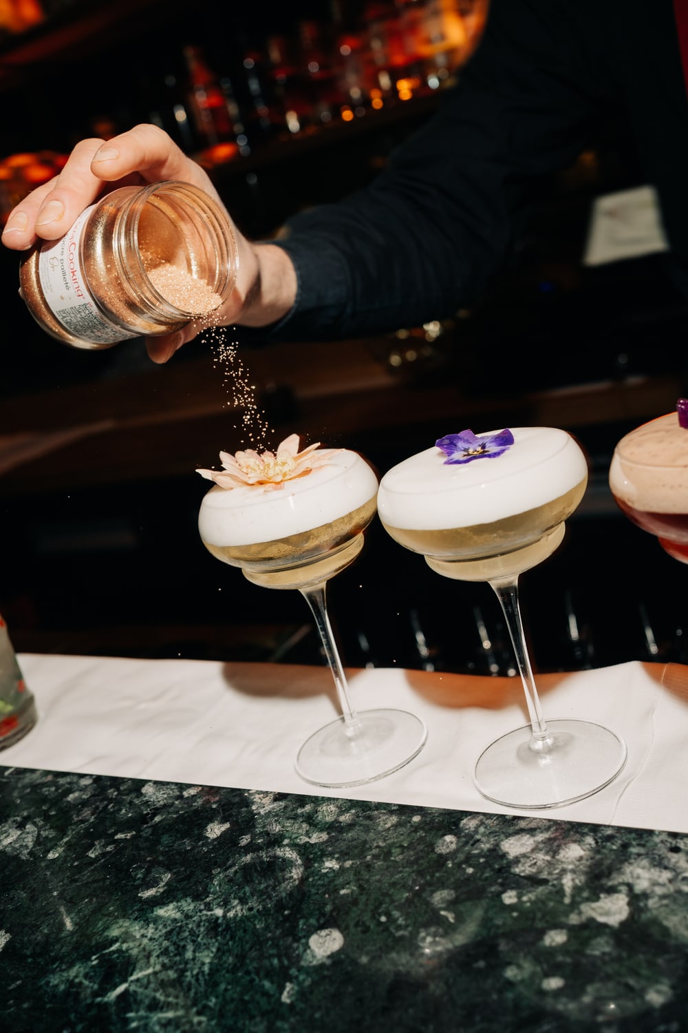 Two cocktails at the bar, finished with an edible flower and a dusting of spice